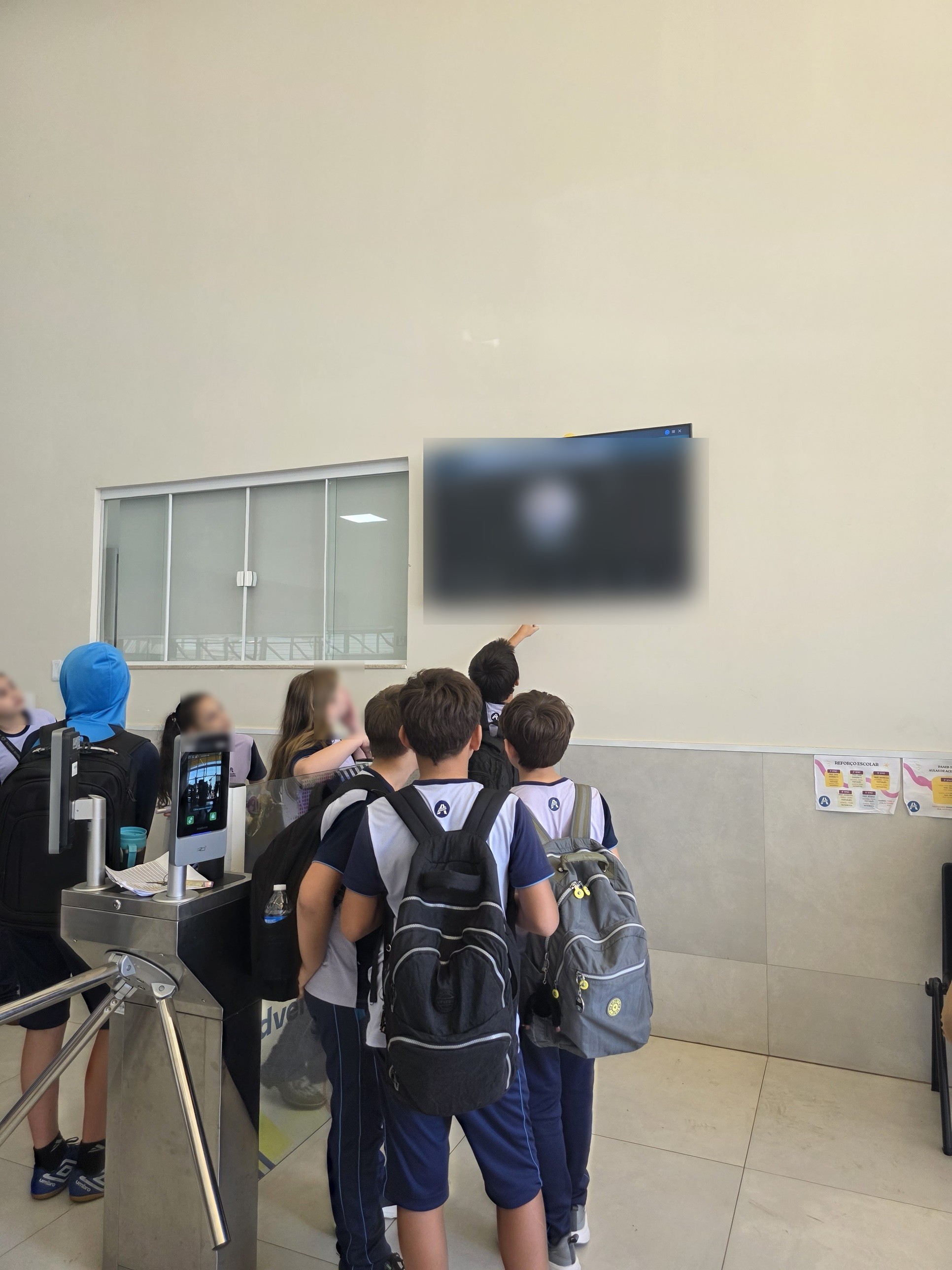 Alunos em frente à TV de chamada na portaria da escola